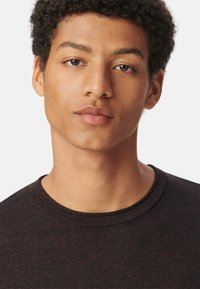 T-shirt noir texturé avec un col rond, présentant un léger motif en côtes. Tissu doux avec des tons de peau naturels visibles sur le visage.