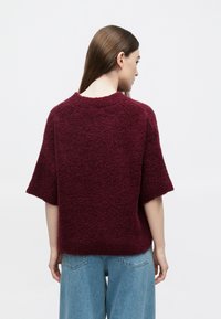 Camisola texturada bordô com mangas curtas, gola redonda e corte solto, combinada com jeans azul claro de perna larga.