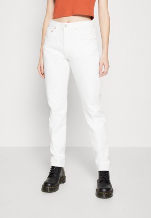 Jeans de denim blanco con un diseño ajustado, bolsillos estándar y acentos de remaches de cobre, combinados con botas negras de cordones.