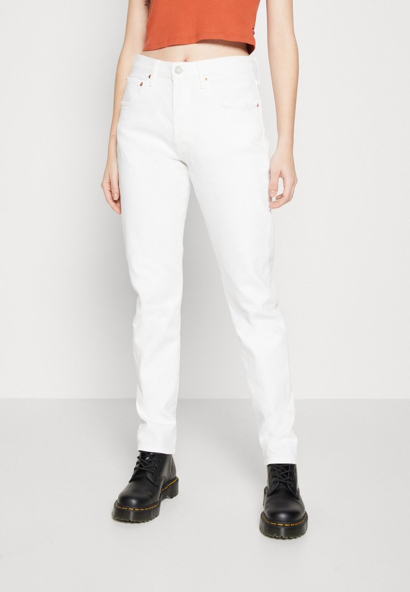 Jeans de denim blanco con un diseño ajustado, bolsillos estándar y acentos de remaches de cobre, combinados con botas negras de cordones.