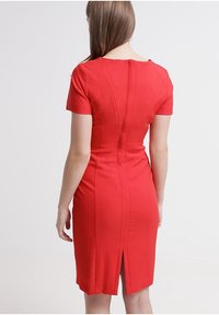 Rode nauwsluitende jurk met korte mouwen, minimalistisch ontwerp, gestructureerde stof, achterste splitdetail en naadtoevoegingen voor vormdefinitie.