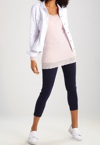 Valkoinen denim-takki vaaleanpunaisen pitsireunalla varustetun tanktopin päällä, yhdistettynä tummansinisiin nilkkatrikoisiin ja valkoisiin liukuvaan kenkiin. Silkkiset pinnat.