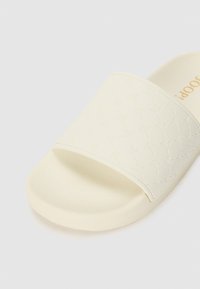 Witte schuimsandalen gemaakt van gestructureerd materiaal met een patroonriem. Beschikt over een gevoerd voetbed en een gladde zool.