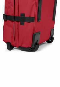 Red wheeled suitcase with a textured fabric exterior, black plastic accents, and secure strap. Features smooth-rolling wheels for mobility.