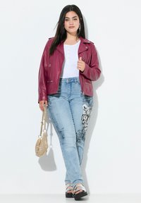 Chaqueta de cuero burdeos, camiseta henley blanca, jeans de mezclilla azul claro con estampado de tigre, sandalias plateadas y un bolso de mano dorado con cuentas.