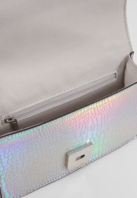 Iriserende pung med slangeskindsstruktur, sølv hardware, magnetisk lukning og en lille lynlåslomme indeni. Foret med lyst stof.