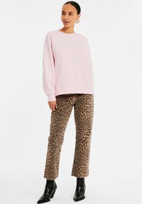 Rosa übergroßer Sweatshirt mit gerippten Bündchen, kombiniert mit braunen, leopardenmuster geraden Hosen und schwarzen Ankle Boots.