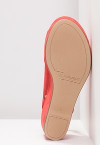 Chaussure plate rouge positionnée semelle vers le haut contre un mur blanc d'angle, avec le nom de la marque « butterflight » embossé sur la semelle marron clair.