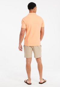 Korte mouwen polo shirt in lichtoranje, gecombineerd met beige shorts. De stof lijkt soepel, met een klassieke kraag en een relaxte pasvorm.