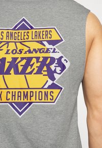 Szara koszulka bez rękawów z żółto-fioletowym logo Los Angeles Lakers oraz dużym, pogrubionym napisem "NBA CHAMPIONS".