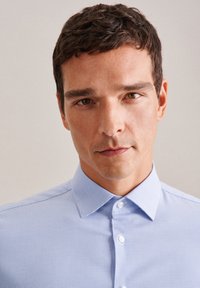 Camicia azzurro chiaro con motivo a quadri, colletto strutturato e tessuto liscio, con bottoni e dettagli di cucitura bianchi.