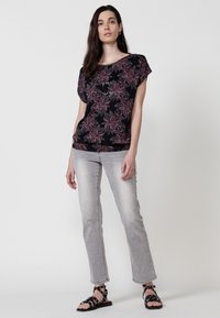 Haut noir à motifs floraux roses et blancs, coupe loose. Associé à un jean gris clair et des sandales noires à lanières. Texture lisse.