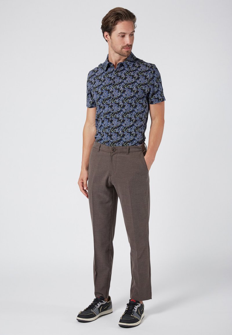 Short-sleeve polo shirt with a blue floral pattern, paired with brown checkered trousers and black sneakers with white soles.