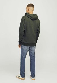 Sudadera verde oscuro de corte holgado, con capucha ajustable y puños acanalados, combinada con jeans de mezclilla azules y zapatillas informales.