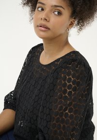 Zwarte kanten top met een bloemenpatroon, textuurstof en een ronde halslijn. De mouwen zijn iets gepoft en tonen delicate details.