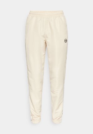 Cream-colored track pants made of smooth fabric. Features an elastic waistband, cuffed ankles, and a black logo on the front.