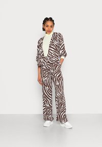 Fato em padrão de zebra castanho e branco, com um casaco solto e calças de perna larga. O modelo usa um pulôver de gola alta verde-claro por baixo.