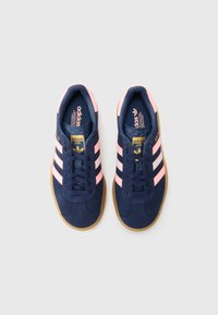 Sapatilhas de camurça azul-marinho com riscas cor-de-rosa e sola de borracha; apresentam um design clássico com atacadores e uma marca na língua e no lado lateral.