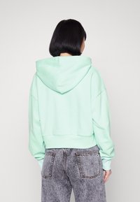Przycięta miętowa bluza z miękkiego materiału z dużym kapturem i opadającymi ramionami, w połączeniu z szarymi dżinsami o wysokim stanem.
