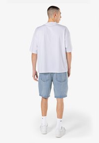 Hvit bomullst-skjorte med korte ermer, kombinert med lyseblå denimshorts. Antrekket har en avslappet passform og klassisk design.