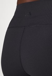 Sorte ribbede leggings med høy liv, kontrasterende sømmer og en liten logo på livet. Mykt, elastisk stoff.