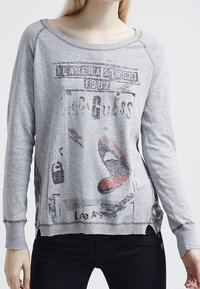 Sudadera gris claro con un escote amplio, mangas raglán y un estampado gráfico que presenta letras en negrita y un diseño de labios rojos.
