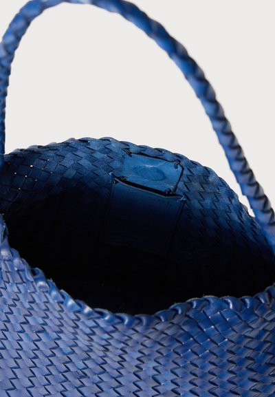 Δερμάτινη τσάντα σε μπλε απόχρωση, υφαμένη με υφή, με ανθεκτικό χερούλι και εσωτερική ετικέτα, κεκλιμένη στην κορυφή.