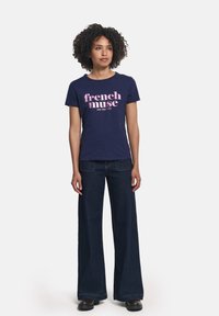 Camiseta de algodón azul marino con texto rosa "musa francesa" y "un paso 1995", combinada con pantalones vaqueros de pierna ancha de mezclilla oscura.