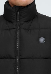 Must must jacket kõrge kraega, ees tõmblukk ja rinnal logo märk. Valmistatud kergest ja polsterdatud materjalist.