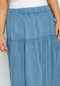 Ljusblå maxiklänning av mjukt, flytande tyg, med en elastisk midja och en lagerdesign med samlade sektioner.