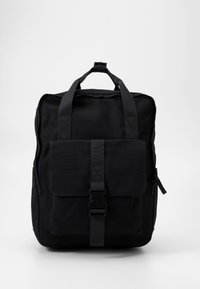 Sac à dos en toile noire avec une poche à rabat à l'avant, des bretelles ajustables et une poignée supérieure. Présente une forme rectangulaire et un tissu texturé.