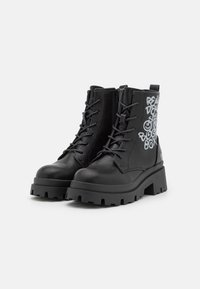 Bottes noires en cuir montantes avec une semelle épaisse, un laçage à l'avant et une fermeture éclair sur le côté. Le côté extérieur présente un texte graphique blanc.