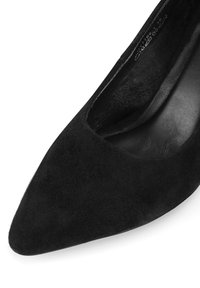 Pantofii negri din suede, cu vârful ascuțit și un interior elegant. Suprafața este moale și mată, având o curbură subtilă de-a lungul deschiderii.