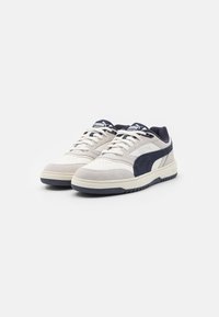 Sneakers bianchi e blu marino realizzati con una combinazione di pelle liscia e camoscio, punta perforata, suola intermedia spessa e suola in gomma testurizzata.