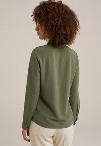Majica z dolgimi rokavi v olivno zeleni barvi, narejena iz teksturirane tkanine, z sproščenim krojem, ovratnikom in detajli gumbov na manšetah.