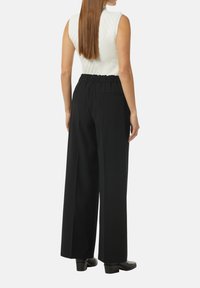 Black wide-leg pants with an elastic waistband, two side pockets, and a smooth fabric texture, paired with a fitted white sleeveless top.