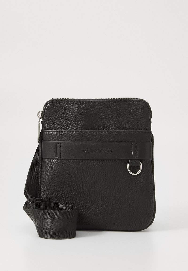 Černá přes rameno nositelná taška z texturované kůže, se zipem, předním popruhem s logem a kovovým kroužkem jako akcentem. Nastavitelný popruh pro všestranné nošení.