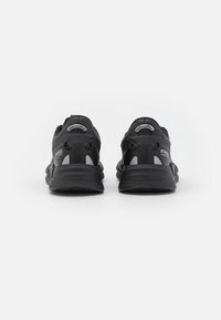 Scarpe sportive nere con un upper testurizzato, dettagli riflettenti e suole imbottite. La parte posteriore presenta un elastico per facilitare la calzata e un marchio distintivo.