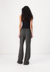 Débardeur noir associé à un pantalon large à rayures verticales noires et gris. Tissu doux et coupe décontractée.
