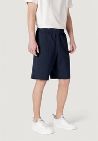 Shorts bleu marine en tissu respirant, dotés d'une taille élastique et d'une coupe décontractée. Associés à des baskets blanches pour le contraste.