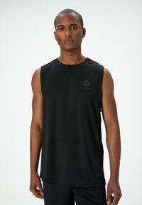 Svart ärmlös träningströja tillverkad av mjukt, lätt material, med en subtil logotyp på bröstet. Rak skärning.