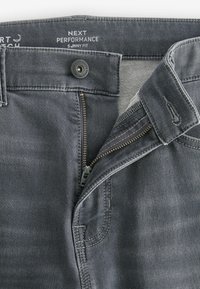 Jeans din denim gri cu fermoar și închidere cu buton. Caracteristicile includ cusături contrastante, o textură fină și un design cu croială dreaptă.