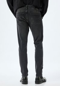 Jeans de corte slim en gris oscuro, con una textura suave, cinco bolsillos y detalles en la parte trasera. Combinados con botas negras de tobillo.