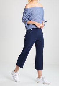 Lys blå off-the-shoulder top med opkrøllede ærmer, parret med marineblå cropped bukser med knapdetaljer og hvide sportssko.