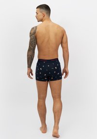 Herrars marinblå boxer shorts med röd midja, prydda med ett blommönster och polkagriskäppar. Sittande design, medelhög längd.