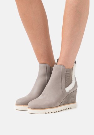 Bottes chelsea grises à talon avec une texture lisse, des panneaux élastiques sur les côtés et une garniture en fausse fourrure, dotées d'une semelle extérieure blanche contrastante.