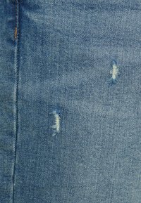Tecido de denim azul com duas áreas desgastadas e bordas desfiadas. A textura está ligeiramente desbotada, apresentando os padrões típicos do entrelaçado do denim.