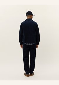 Dunkelblaue Cordjacke und passende Hose, mit einem lässigen Schnitt und weichem Stoff. Akzentuiert mit einem karierten Hemd darunter.