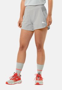 Lichtgrijze sportshorts met een platte tailleband, zijzakken en een contrasterend logo. Gecombineerd met grijze en oranje schoenen en sokken.