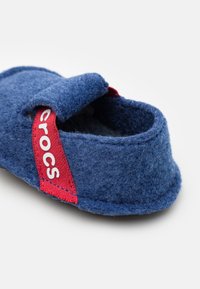 Scarpa blu in feltro da indossare, con un cinturino rosso con il logo Crocs, forma arrotondata, texture morbida e design aperto, adatta per l'uso interno.